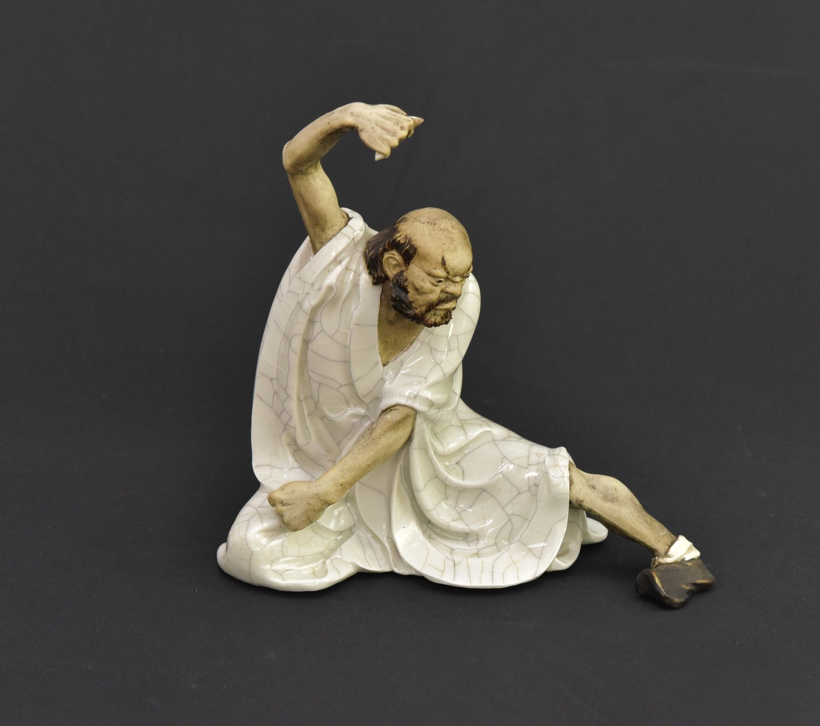 Exquisite ceramic figurine depicts a seated figure in a dynamic pose